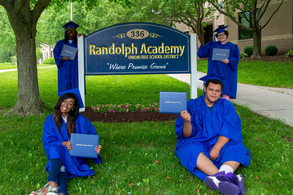 grads pose in front of school sign