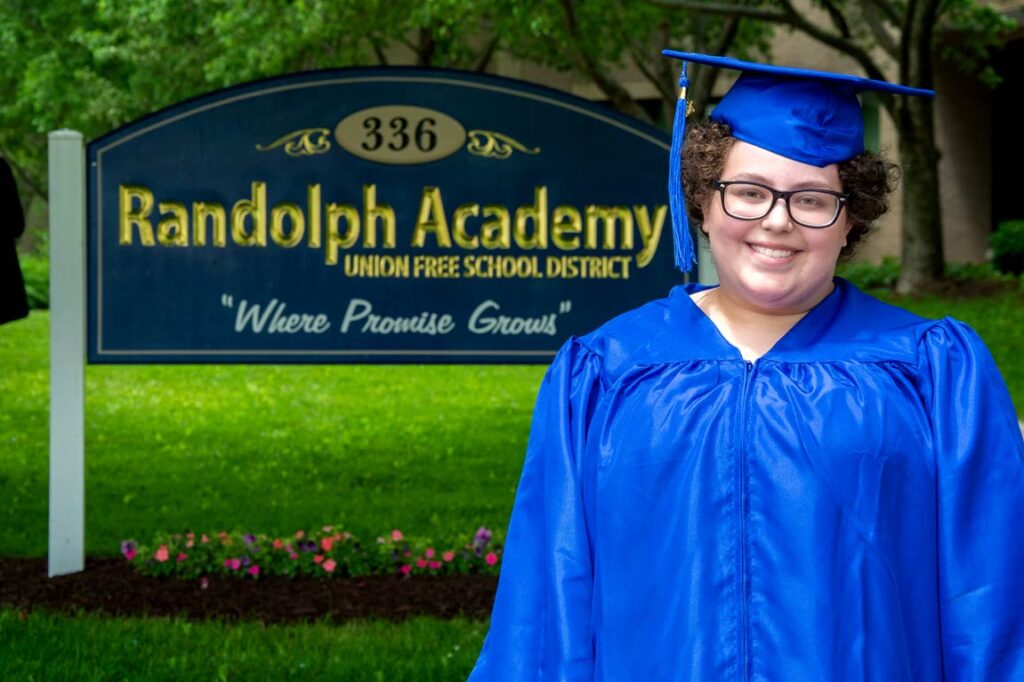 graduate poses in front of Randolph school entrance sign